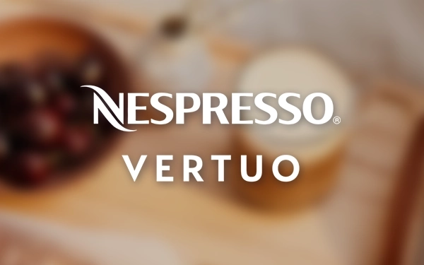 Логотип Nespresso Vertuo на розмитому фоні з чашкою кави та кавовими зернами