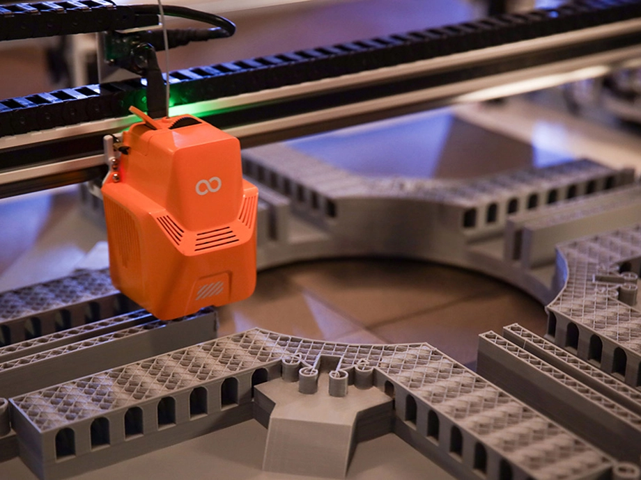 Внутрішня частина 3D-принтера за роботою, з надрукованими архітектурними елементами, видимими на робочій підлозі.